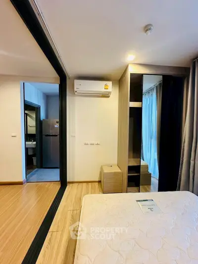 Modern bedroom with wooden flooring, air conditioning, and sliding glass doors leading to a compact kitchen.