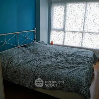 Cozy bedroom with blue walls and patterned bedding, featuring a large window with floral curtains.