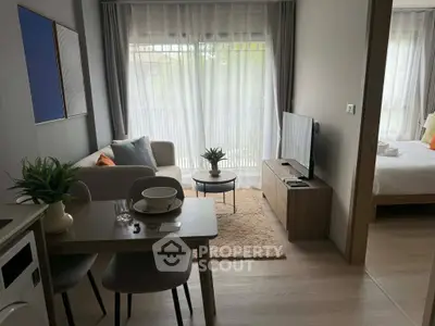 Modern open-plan living room with cozy decor and natural light, featuring a dining area and view into the bedroom.