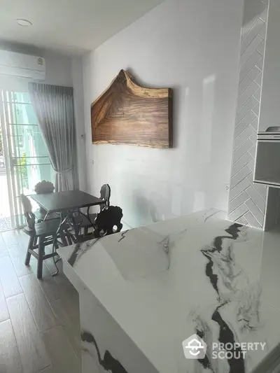 Modern kitchen with marble countertop and wooden wall art, featuring a cozy dining area by the window.