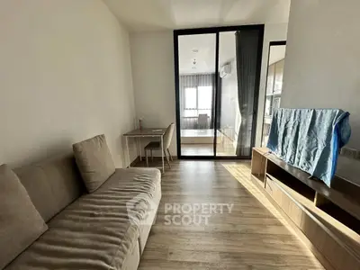 Modern living room with cozy sofa and wooden flooring, featuring a glass partition to a bright bedroom.