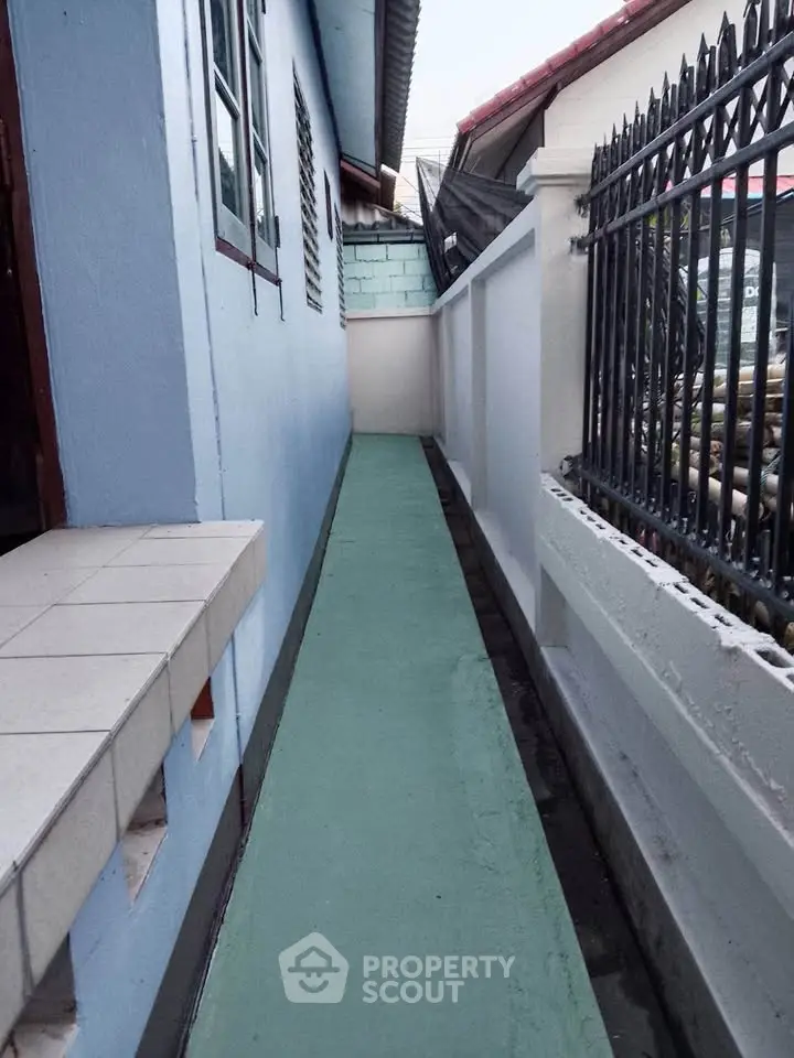 Narrow side pathway beside a residential building with blue walls and tiled ledge.