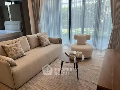 Elegant living room with cozy sofa, stylish armchair, and garden view through large windows.