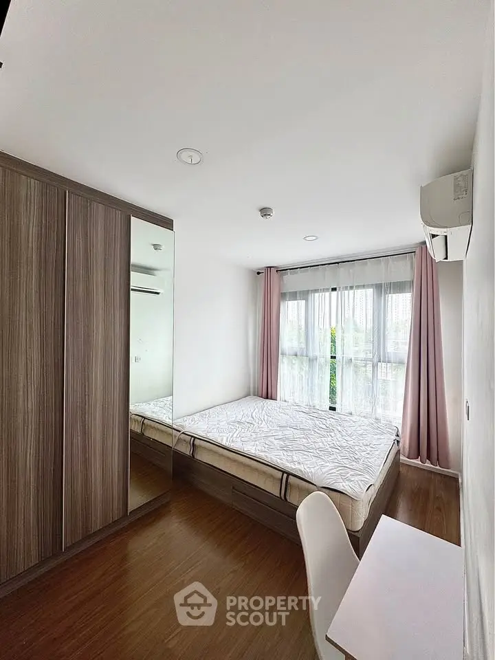 Modern bedroom with large window, wooden flooring, and built-in wardrobe in a stylish apartment.