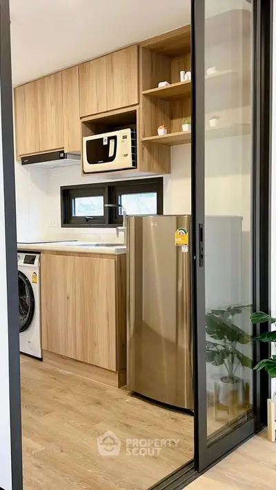 Modern kitchen with wooden cabinets, stainless steel fridge, and washing machine in compact layout.