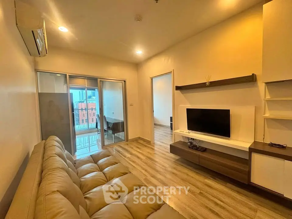 Modern living room with cozy sofa and TV, featuring a balcony view and stylish wooden flooring.