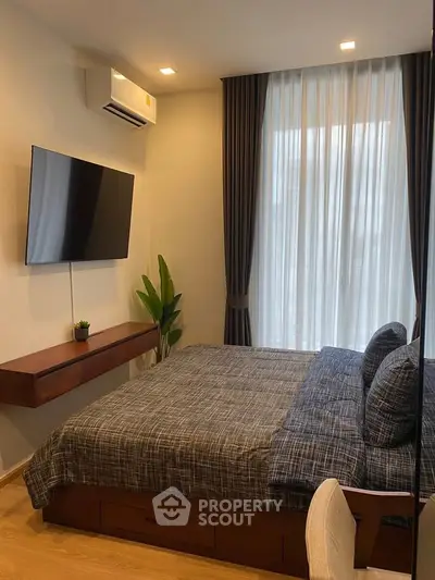 Modern bedroom with stylish decor, featuring a wall-mounted TV and large window with elegant curtains.