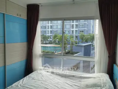 Cozy bedroom with large window overlooking pool and modern apartment complex.