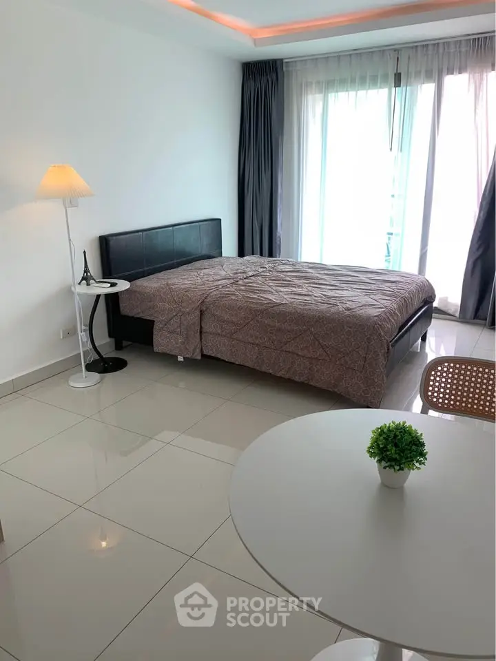 Modern bedroom with sleek design, featuring a cozy bed, stylish lamp, and natural light from large windows.