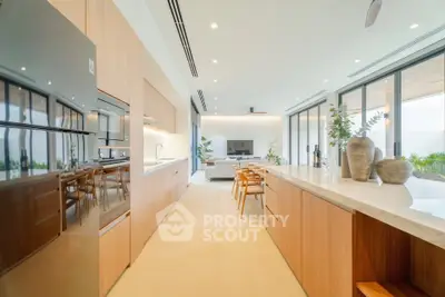 Spacious modern kitchen with open layout and sleek wooden cabinetry, leading to a bright living area.
