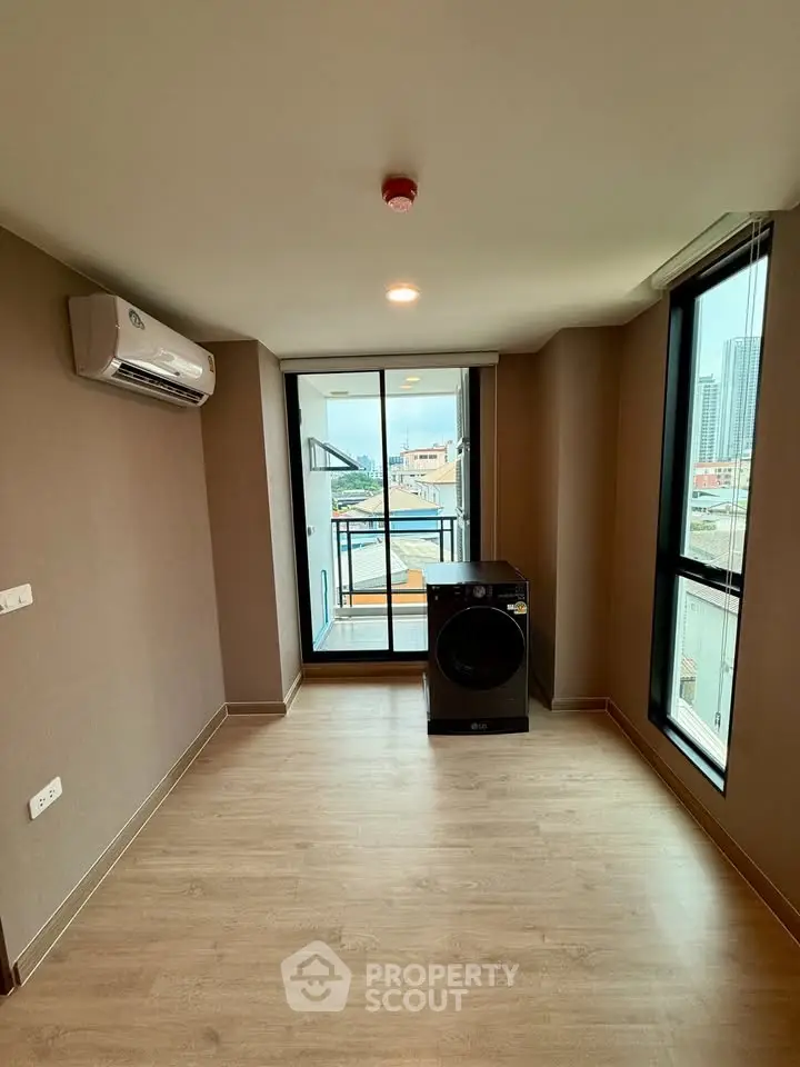 Modern unfurnished room with air conditioning and washer, featuring large windows and balcony access.