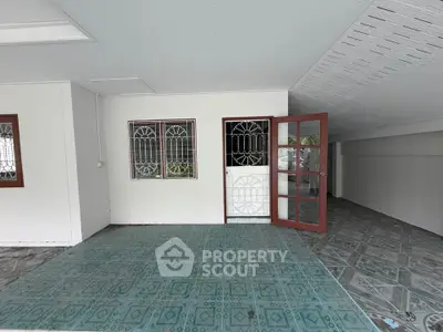 Spacious covered patio with tiled flooring and decorative metal door, perfect for outdoor relaxation.