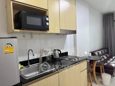Modern kitchen with microwave, fridge, and cozy living area in stylish apartment.