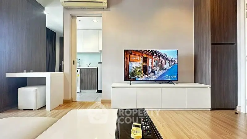 Modern living room with sleek TV setup and open kitchen layout in stylish apartment.