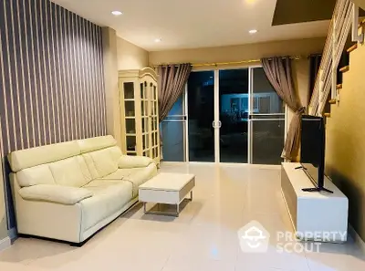 Elegant living room with glossy white tiles, cream sofa set, and large glass doors leading to a balcony, offering a modern and spacious ambiance.