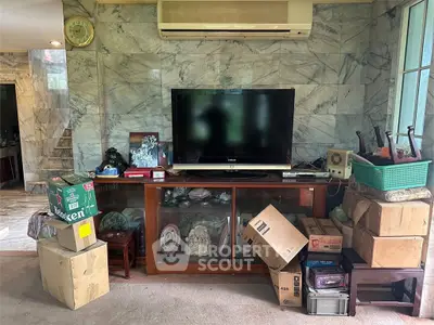 Spacious living room with marble walls and air conditioning, featuring a TV and various boxes.