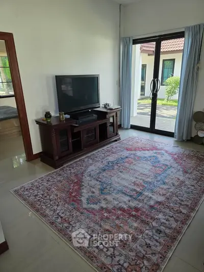 Charming living room with elegant rug and large TV, featuring natural light from sliding glass doors.