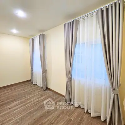 Spacious room with elegant curtains and wooden flooring, perfect for a cozy living space.