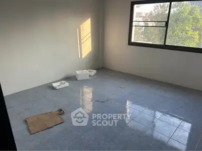 Spacious empty room with blue tiled floor and large window offering natural light.