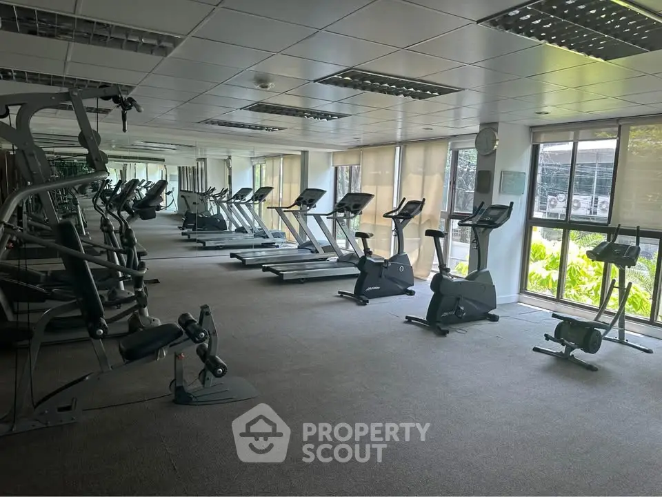 Spacious gym with modern equipment and large windows in a residential building.
