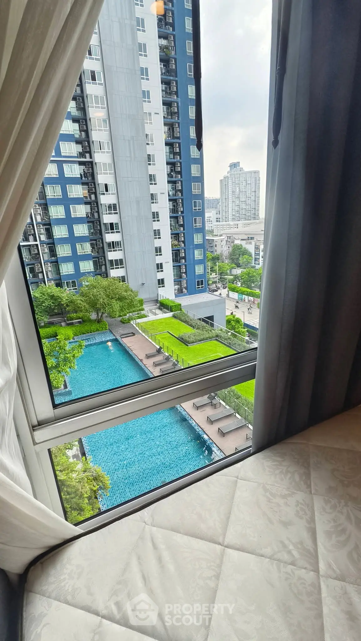 Stunning city view from a high-rise apartment window overlooking a luxurious pool and modern buildings.