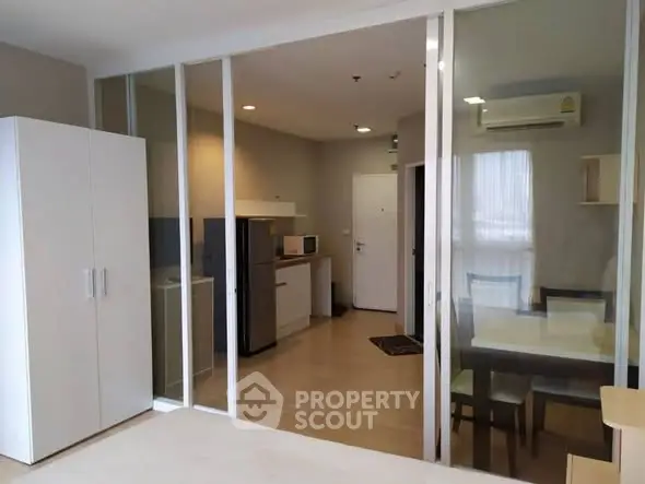 Modern apartment interior with glass partition, dining area, and kitchen appliances.