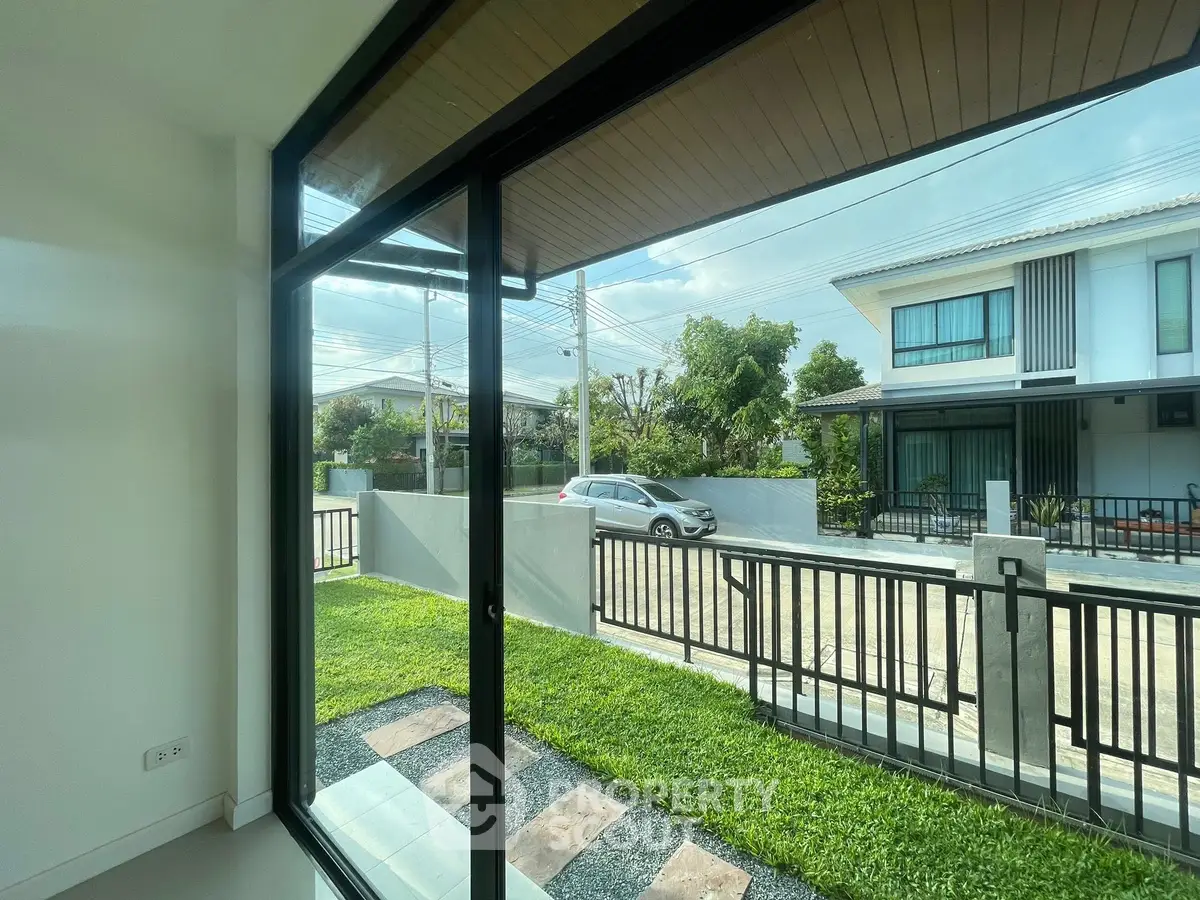 Modern home with large glass doors opening to a lush green garden and street view.