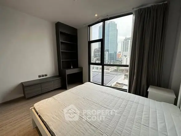 Modern bedroom with city view, featuring large windows and sleek furnishings.