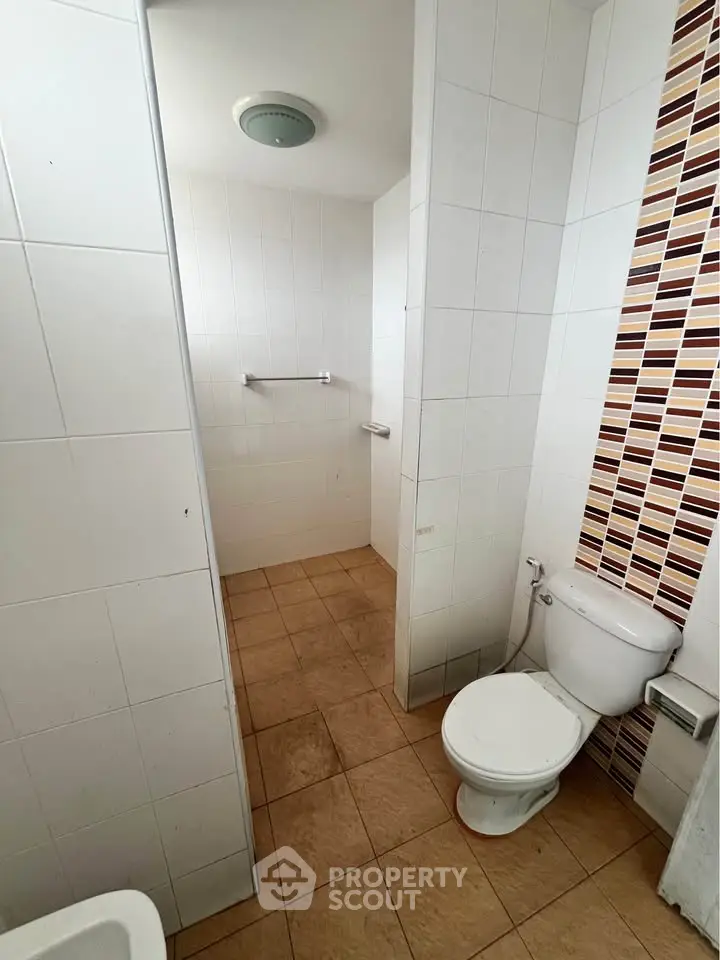 Compact bathroom with tiled walls and floor, featuring a toilet and shower area.