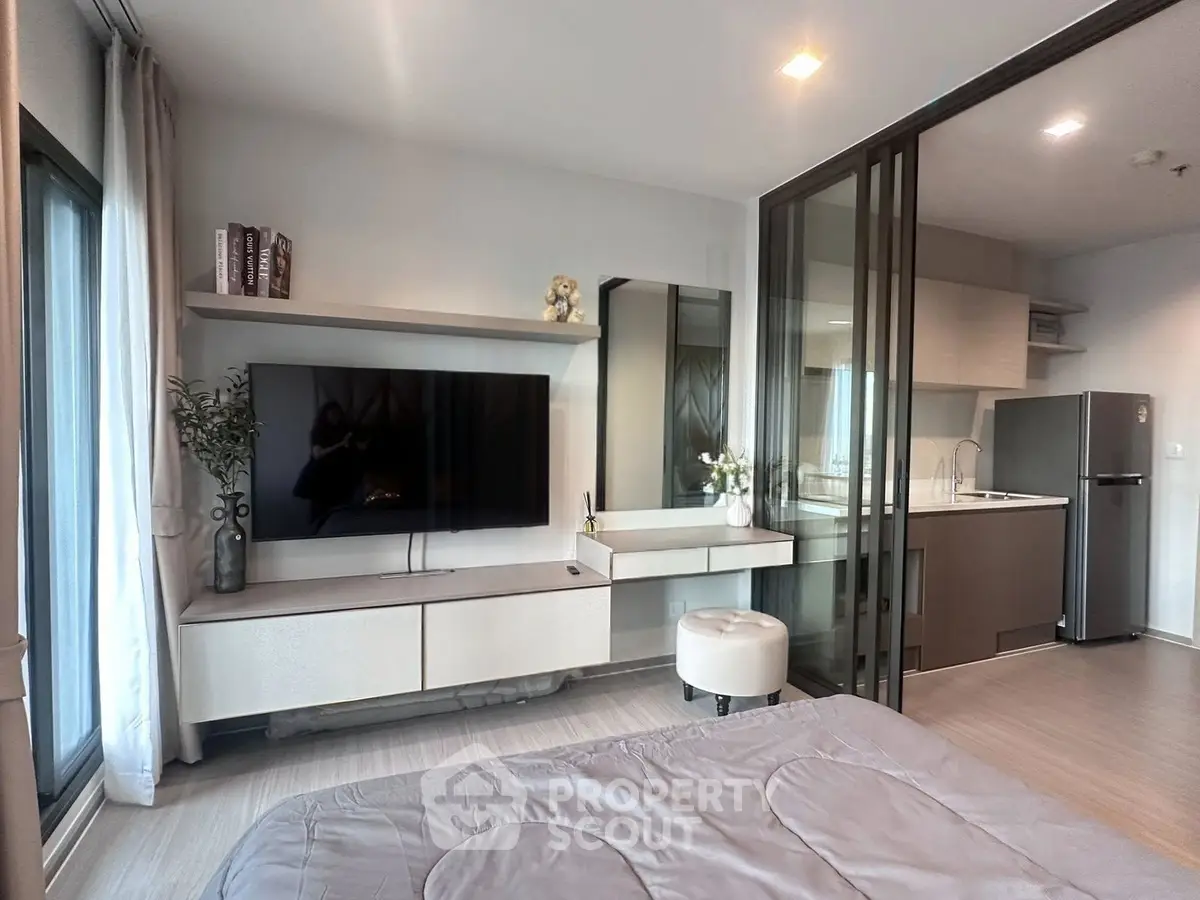 Modern studio apartment with sleek kitchen and cozy living area, featuring a large TV and stylish decor.