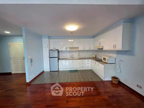 Spacious kitchen with modern appliances and wooden flooring in a bright apartment.