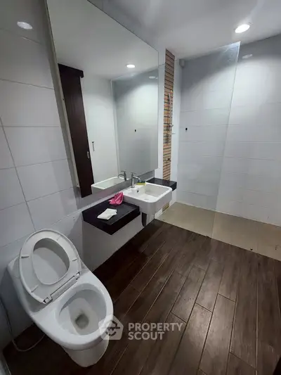 Modern bathroom with sleek fixtures and wooden flooring, featuring a spacious shower area and large mirror.