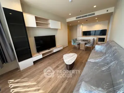 Modern living room with open kitchen, featuring sleek furniture and hardwood floors.