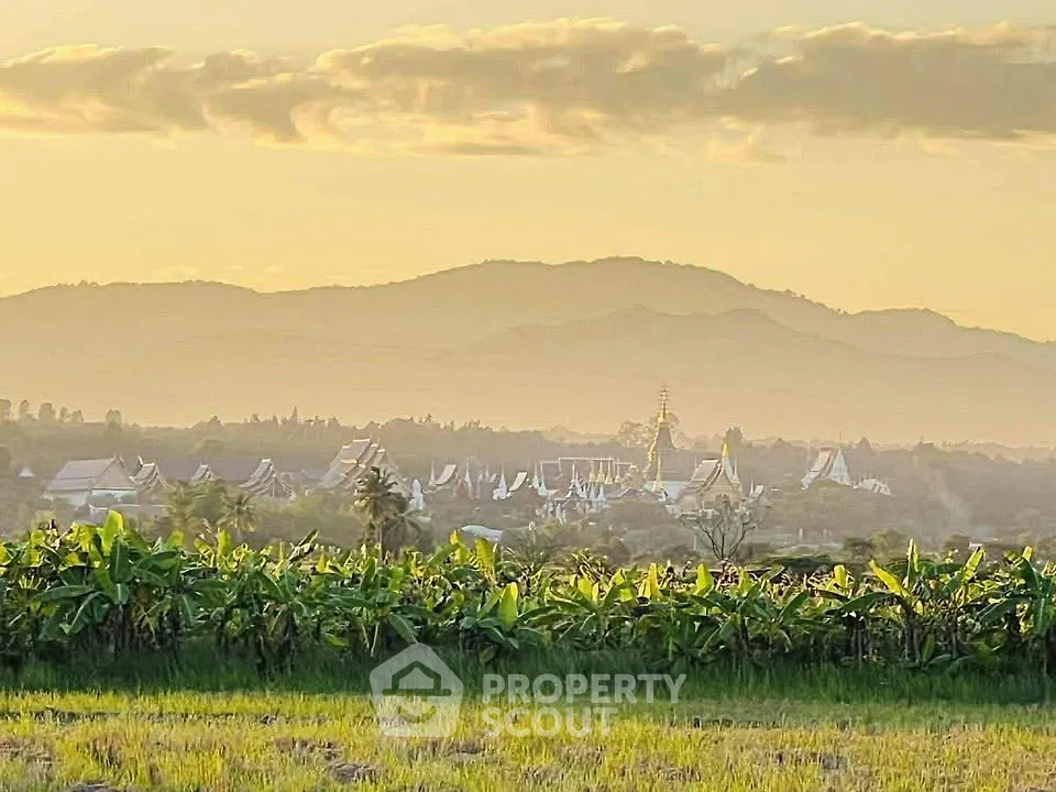 Scenic view of lush green fields with distant mountains and traditional architecture at sunset.