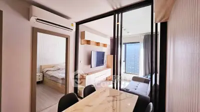 Modern apartment interior with open living room and bedroom, featuring sleek furniture and large window view.