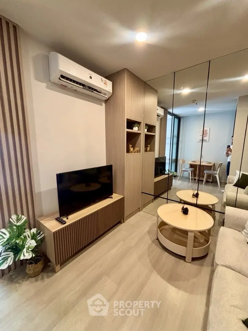 Modern living room with mirrored wall, sleek furniture, and cozy dining area in a stylish apartment.