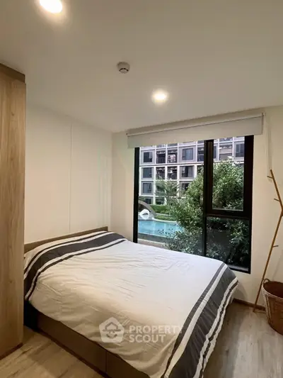 Cozy bedroom with a view of lush greenery and modern building exterior, featuring a comfortable bed and natural light.
