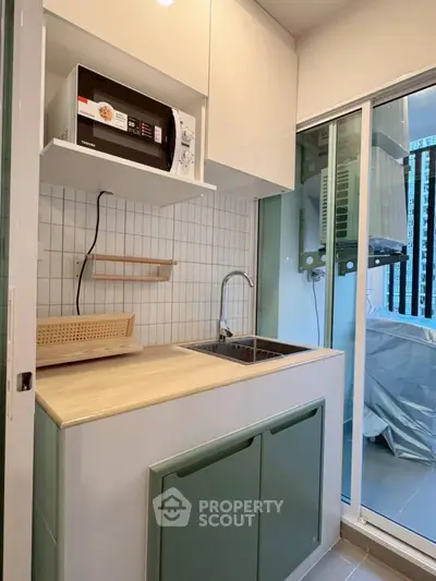 Compact kitchen with modern design and balcony view, featuring a microwave and sleek cabinetry.