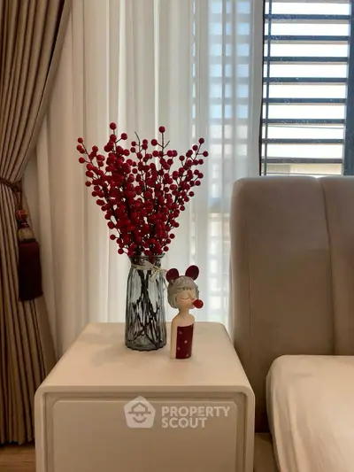 Elegant bedroom corner with plush bed and stylish decor, featuring a vase of red berries on a modern nightstand.