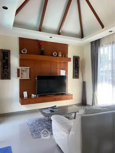Elegant living room with vaulted ceiling, modern decor, and large TV, perfect for relaxation and entertainment.