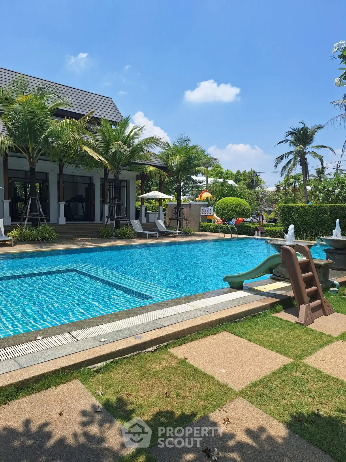 Luxurious tropical villa with sparkling pool and lush palm trees under a clear blue sky.