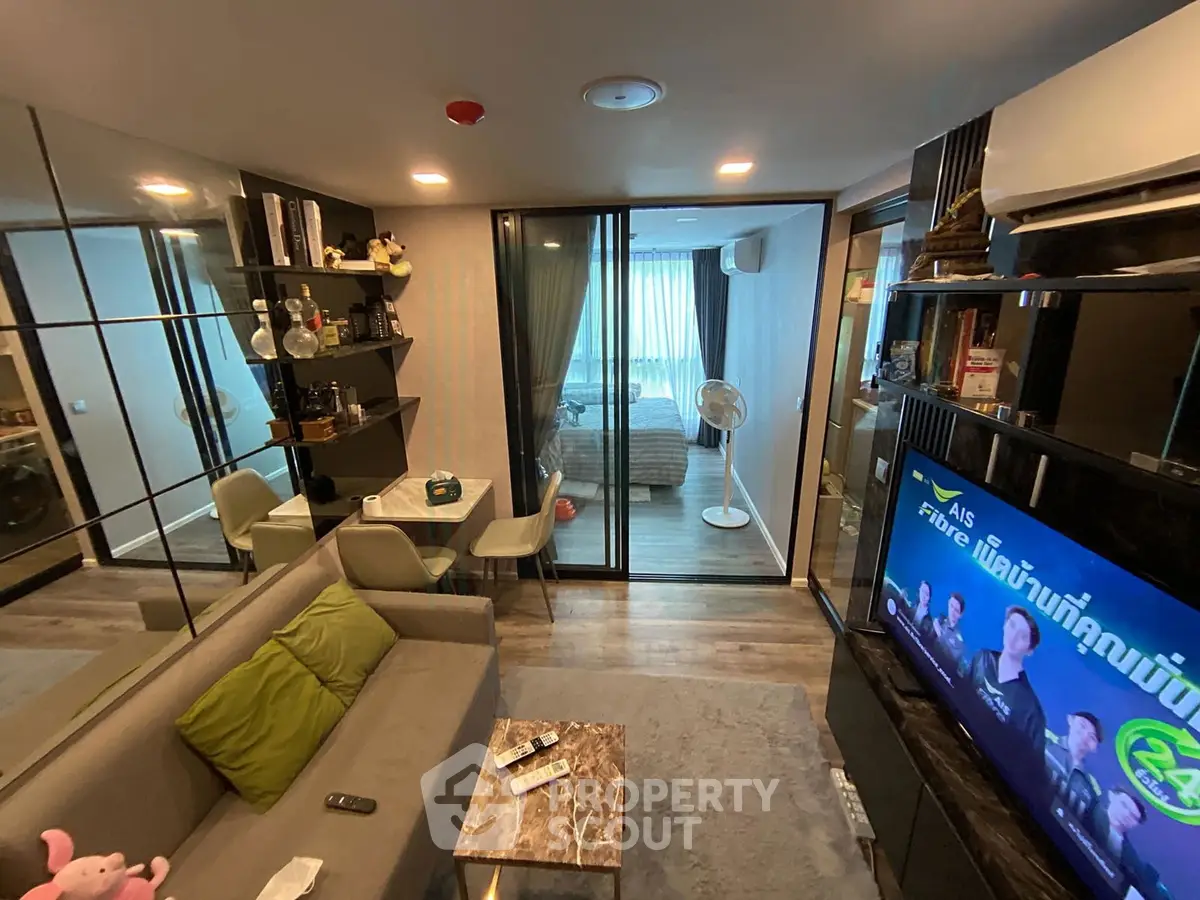 Modern living room with stylish decor and glass partitions leading to a cozy bedroom.