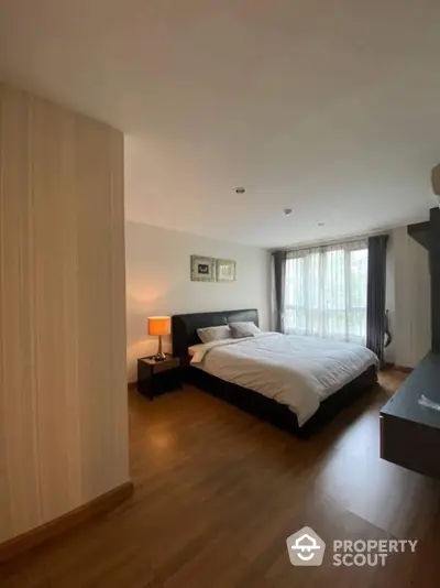 Spacious bedroom with polished hardwood floors, modern furnishings, and ample natural light filtering through sheer curtains, creating a serene and inviting atmosphere.