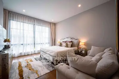 Elegant bedroom with cozy seating area and large window for natural light.