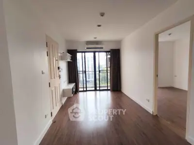 Spacious living room with wooden flooring and large windows offering natural light and city view.