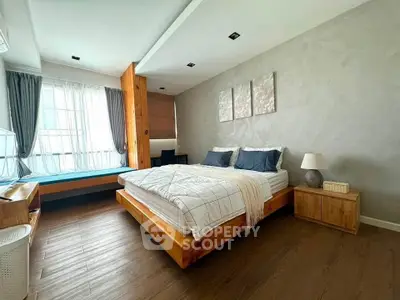 Spacious modern bedroom with wooden flooring and large window for natural light.