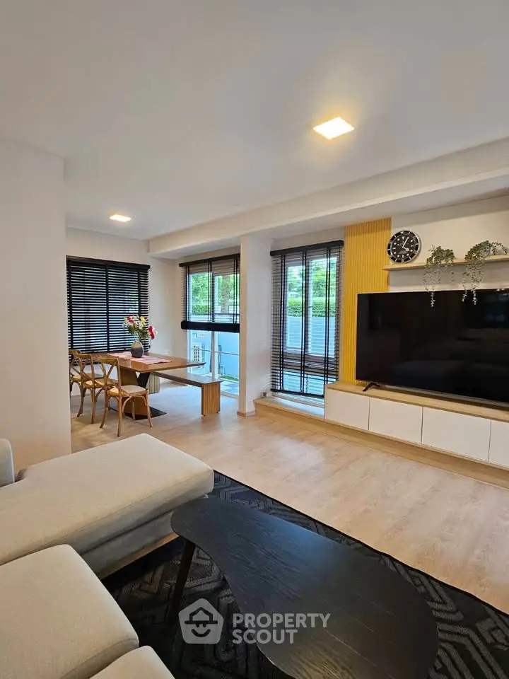 Modern living room with large TV, stylish furniture, and dining area, featuring natural light and contemporary design.