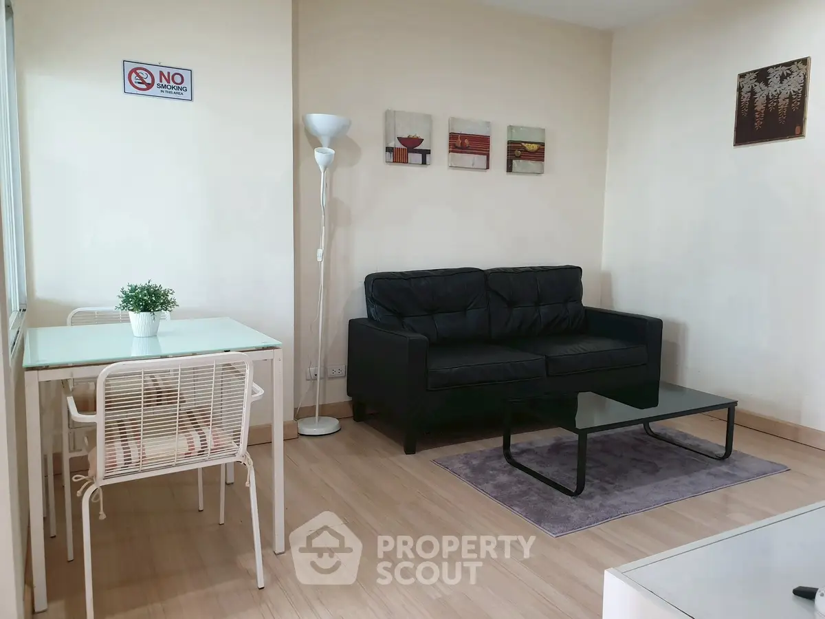 Modern living room with black sofa, glass coffee table, and dining area in a cozy apartment.