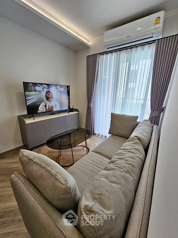 Modern living room with stylish sofa, TV, and air conditioning, featuring elegant curtains and wooden flooring.