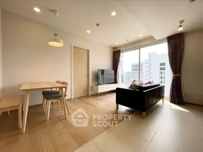 Modern living room with wooden flooring, cozy seating, and large windows offering city views.